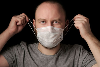 A young man with a beard and blue eyes puts on a medical mask to protect himself 