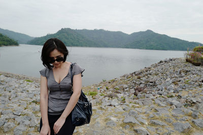 Young woman wearing sunglasses standing on shore against mountains