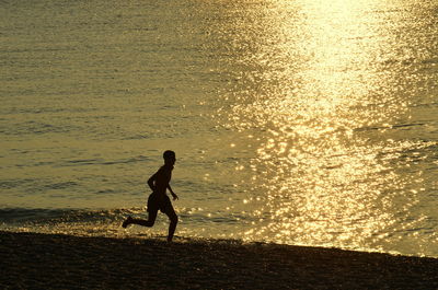 Silhouette man standing on beach against sky during sunset