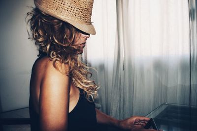 Close-up of woman wearing hat while using phone at home