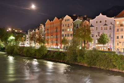 Illuminated buildings by river against sky at night