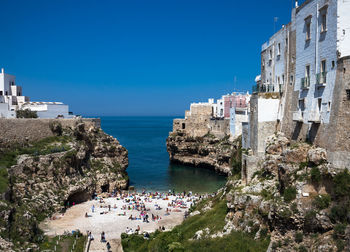 People on rocks by sea against buildings in city