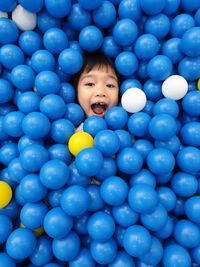 High angle portrait of boy with mouth open lying amidst balls