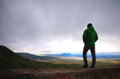 A man traveling on foot, standing in a bright jacket on top of o