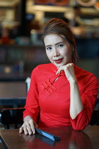 Portrait of smiling woman wearing red dress sitting at table in cafe