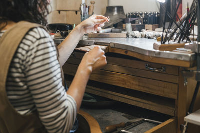 Midsection of student shaping ring while sitting by table in workshop