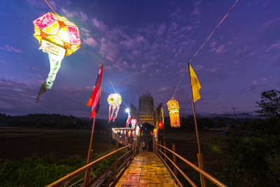 People at illuminated bridge against sky at night