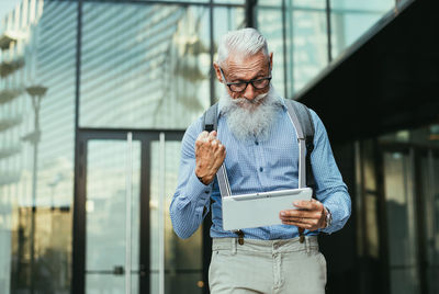 Senior hipster holding digital tablet against building