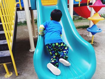 Rear view of boy sitting on slide at playground