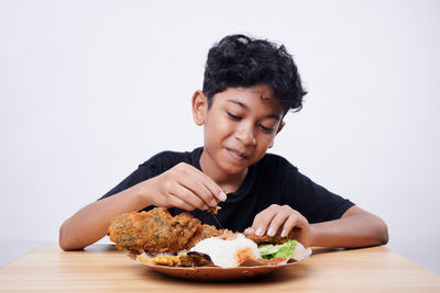 Young woman eating food on table against white background