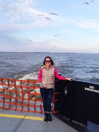 Happy woman standing by no smoking sign at ferry boat against sky