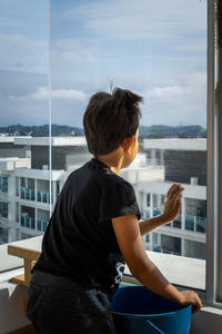 The concept of home apartment cleaning. a boy on the window and wipes with a rag. view from behind.