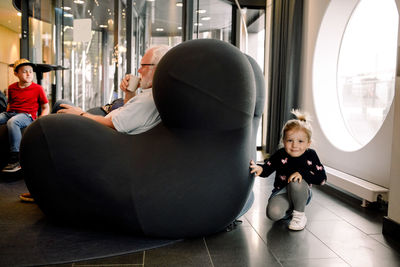 Portrait of smiling girl hiding by armchair in hotel lobby