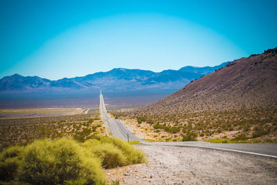 Uneven road of asphalt through death valley national park with hills and mountains at horizon