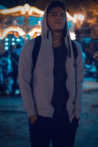 Portrait of young man in hooded jacket standing on street at night