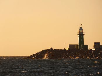 Lighthouse by sea against sky during sunset