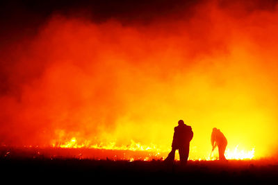 Silhouette firefighters working on burning gassy field