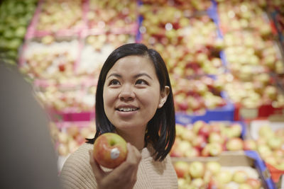 Smiling woman in supermarket holding red and yellow apple