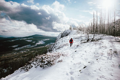 Rear view of man walking on snow against sky during winter