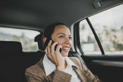 Smiling female entrepreneur talking on phone while traveling in taxi