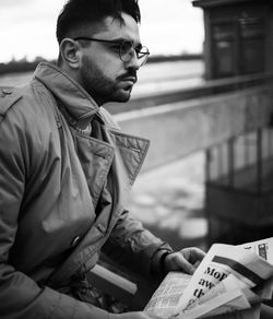 Young businessman reading newspaper in city on bridge in winter.