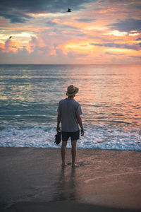 Rear view of man standing on beach during sunset