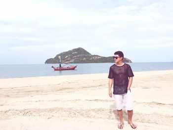 Young man standing on shore against boat moored at sea