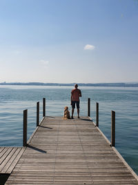 Rear view of man with dog on pier over sea against sky