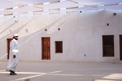 Side view of man walking on footpath by building