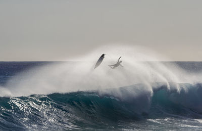 Silhouette man surfing on sea against clear sky