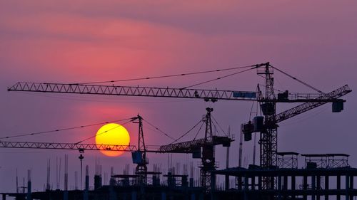 Silhouette cranes against sky during sunset