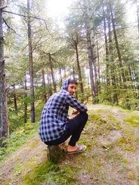 Side view of young man sitting on land in forest