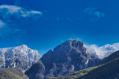 Low angle view of snowcapped mountains against blue sky