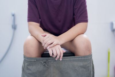 Midsection of man sitting on toilet bowl in bathroom