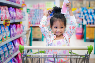 Smiling cute girl holding credit card and bottle while shopping in supermarket