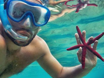 Shirtless man holding starfish while snorkeling in sea
