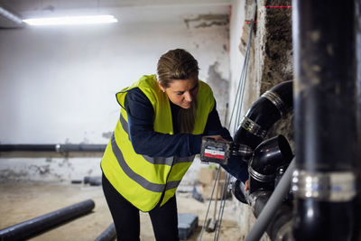 Concentrated female plumber sawing pipe at basement