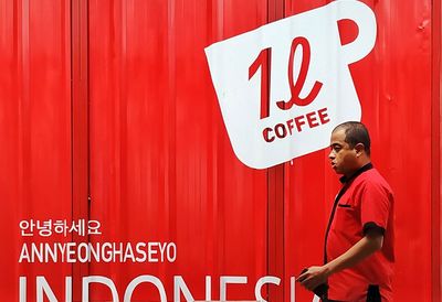 Side view of man standing against red wall