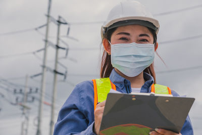 Portrait of engineer wearing mask holding clipboard outdoors