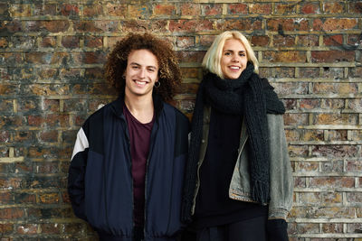 Portrait of smiling young couple against brick wall