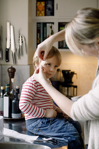 Mother applying bandage on daughter's face in kitchen at home