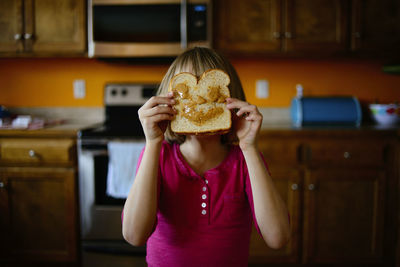 Girl holding bread against her face in kitchen