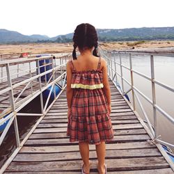 Rear view of girl standing on pier over lake against sky