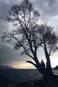 Silhouette of man on tree by sea against sky