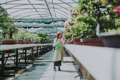 Full length of woman standing by plants in greenhouse