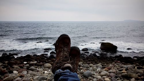 Low section of person on stones at beach against sky