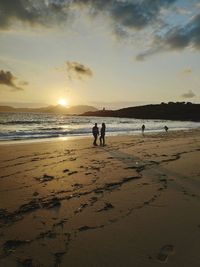 People on beach against sky during sunset