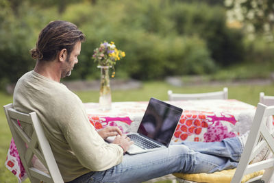 Man using laptop while sitting on chair in back yard