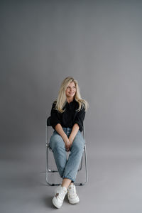 Portrait of young woman sitting on chair against black background