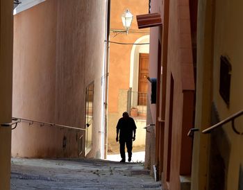 Silhouette man walking in alley amidst buildings 